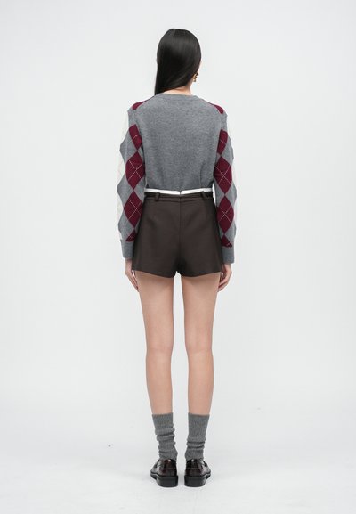 Pletený šedý sveter s marhuľovými a šedými argyle rukávmi, skombinovaný s hnedými nohavicami s vysokým pásom, šedými ponožkami a tmavou obuvou.