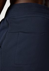 Marineblå bukser laget av et mykt, elastisk stoff. Har en stor, ekstern sidelomme og en elastisk midje for komfort.