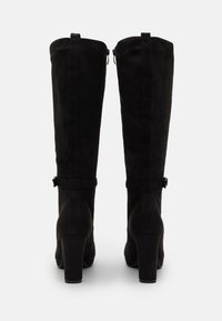 Black suede knee-high boots with a round toe, block heel, and side zipper. Features a strap with a buckle around the ankle.