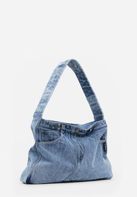 Sac à épaule en tissu denim bleu avec poches de jeans visibles, passants de ceinture, boutons et détails de couture.