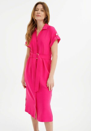 Roze jurk met riem, kraag, korte mouwen en zijsplitten; de textuur van de stof voegt visueel interesse toe.