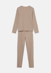 Beige long-sleeve top and matching pants made from soft fabric, featuring frayed hems and a relaxed fit.