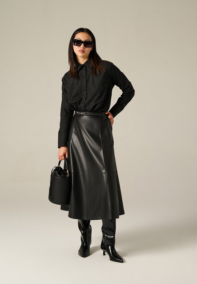 Chemise noire à boutons avec des détails perforés, jupe en cuir noir taille haute, bottes noires jusqu'aux genoux et sac seau noir texturé.