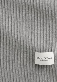 Grijze ribbelgebreide stof met een textuur van verticale lijnen. Inclusief een wit label met "Marc O'Polo" en "EST. IN STOCKHOLM" in zwart gedrukt.