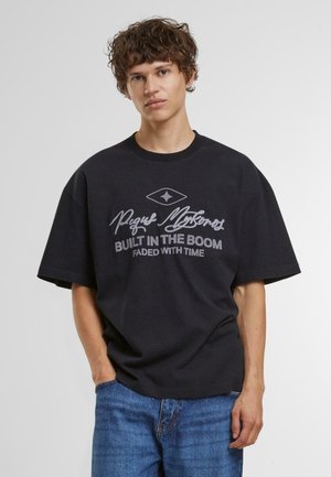 Sort oversized t-shirt lavet af bomuld, med grafisk tekst i hvid. Korte ærmer og en rund halsudskæring. Bæres med blå denim jeans.