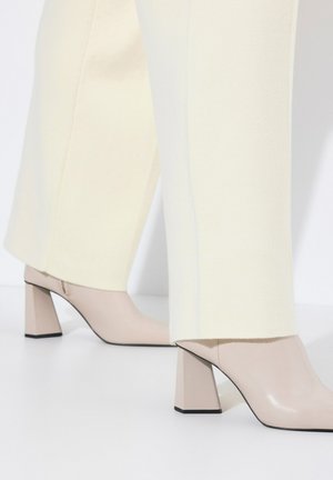 Scarpe beige con tacco a blocco, abbinate a pantaloni su misura color crema. Le scarpe presentano una finitura lucida e una punta affilata.