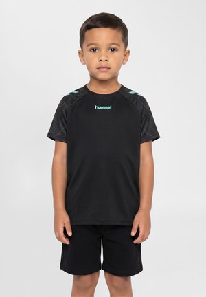 Dreng stående frontalt iført en sort hummel sportst-shirt med mønstrede ærmer og sorte shorts mod en ensfarvet baggrund.