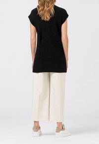 Mustikkakuvioinen neule tunika, hihaton malli, yhdistettynä kermaisiin leveälahkeisiin housuihin ja beigeihin lenkkareihin. Minimalistinen tyyli puhtain linjoin.