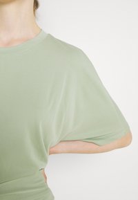 Jasnozielona, oversize koszulka z krótkimi rękawami, wykonana z miękkiego materiału, z okrągłym dekoltem i gładką fakturą. Prosty design, bez widocznych wzorów lub akcentów.