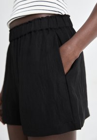 Shorts noirs en tissu texturé avec une taille élastique, dotés de poches latérales et d'une coupe décontractée, présentés de profil.