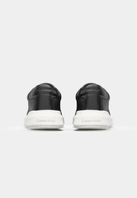 Schwarze Slip-On-Sneaker mit einem glatten Lederoberteil, gepolstertem Kragen und weißer Gummisohle, die das eingeprägte "Calvin Klein"-Branding zeigt.