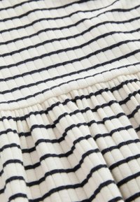 Biała tkanina z czarnymi poziomymi paskami, z prążkowaną teksturą i marszczonym wykończeniem dołu. Widoczny gładki i elastyczny materiał.
