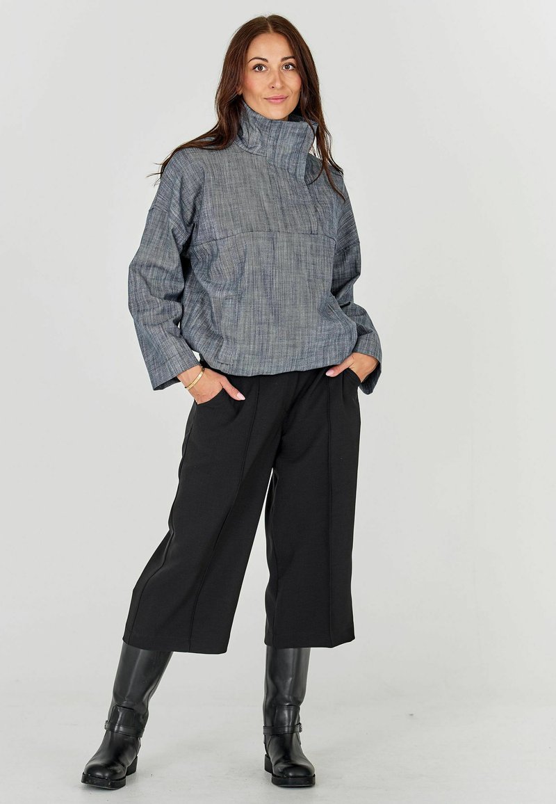 Hall värvi tekstureeritud kootud särk kõrge kraega, koos mustade laia säärega pükstega ja põlvini ulatuvate mustade saapastega. Lihtne disain, lõdva istuvusega.