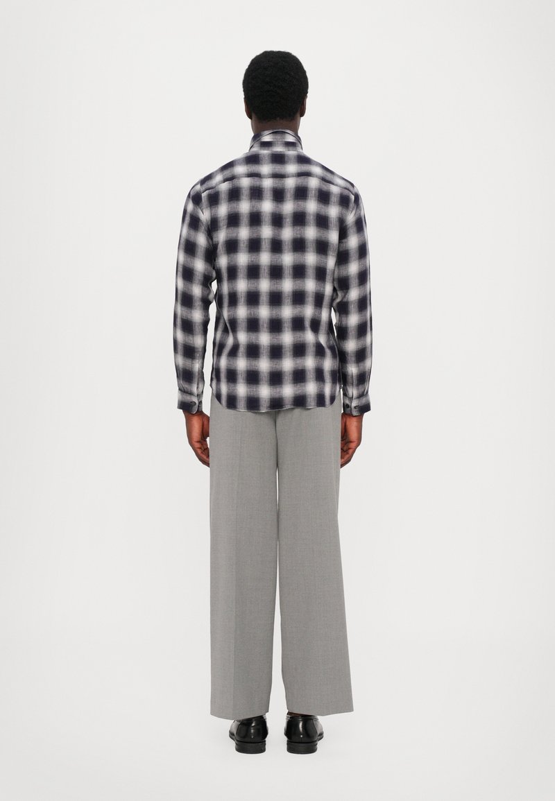 Langsleeve geruite blouse in navy en wit, gecombineerd met wijde grijze broeken en zwarte schoenen, bekeken vanaf de achterkant.