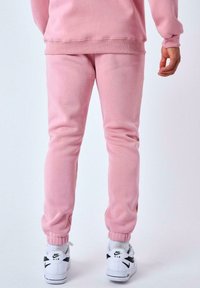 Pantalones de chándal rosas con puños elásticos, hechos de una tela suave, combinados con zapatillas blancas con detalles en negro. Detalle visible en la cinturilla.