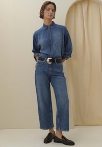 Denim shirt with a collar, button front, and a chest pocket paired with wide-leg jeans, secured with a black belt featuring a round silver buckle.