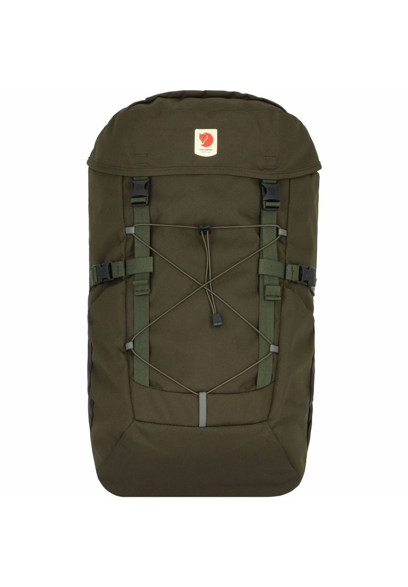 Dark green backpack made of durable fabric, featuring a top flap, adjustable straps, and bungee cord for extra storage. Logo patch on front.