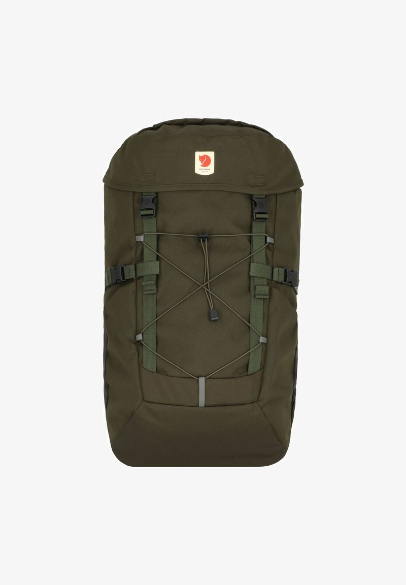 Sac à dos vert foncé en tissu résistant, avec un rabat supérieur, des bretelles réglables et un cordon élastique pour un rangement supplémentaire. Patch de logo à l'avant.