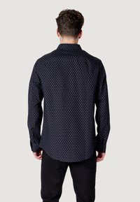 Camicia blu navy con motivo a pois bianchi, maniche lunghe e colletto classico, realizzata in un tessuto morbido.