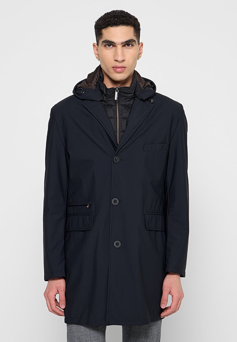 Marineblauer wasserdichter Mantel mit abnehmbarem Kapuzen, Knopfverschluss und zwei Fronttaschen. Verfügt über ein schlankes Design und ein kontrastierendes Innenfutter.
