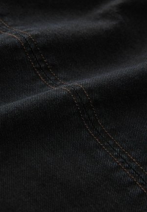 Svart denimtyg med en fin textur, som har synlig orange sömnad längs sömmarna, vilket skapar en subtil kontrast i designen.