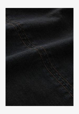 Tessuto denim nero con una fine trama, caratterizzato da cuciture arancioni visibili lungo le cuciture, creando un sottile contrasto nel design.