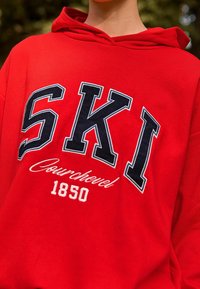 Sudadera roja con gran lettering en navy "SKI", texto más pequeño en blanco "Courchevel" y "1850", elaborada en suave tejido de algodón.