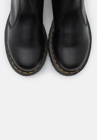 Cizme negre din piele până la gleznă, cu un finisaj neted, vârf rotund și cusături galbene contrastante pe talpă. Vedere din față arată o formă uniformă.