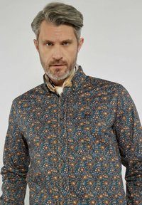 Koszula w niebieskim kolorze z kwiatowym wzorem, z zapięciem na guziki i kołnierzykiem. Materiał wydaje się mieć teksturę z gładkim wykończeniem.