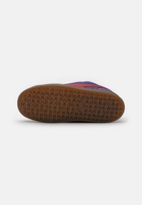 Schoenzool met een getextureerd bruin rubberen oppervlak met een rasterpatroon. Accentkleuren zijn blauw en rood op het bovenste gedeelte.