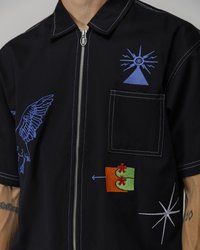 Black short-sleeve shirt with blue and multicolored embroidery, featuring a zip front, a chest pocket, and contrasting stitching details.