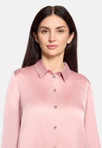 Różowa satynowa koszula z klasycznym kołnierzem, długimi rękawami oraz zapięciem na guziki z przodu. Charakteryzuje się gładką fakturą i subtelnym połyskiem.