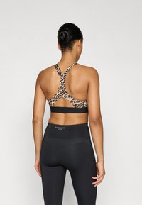 Αθλητικό σουτιέν με σχέδιο λεοπάρ και σχεδιασμό με χιαστί στην πλάτη, συνδυασμένο με ψηλόμεσα μαύρα κολάν με λεπτομέρεια λογότυπου.