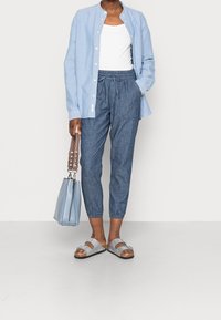 Chemise bleue claire à boutons sur un débardeur blanc, associée à un pantalon tapered bleu foncé, des sandales grises et un sac à main bleu clair.