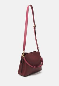 Sac à épaule en cuir bordeaux avec une texture lisse, une longue bandoulière réglable et des accents en or. Détails de poche courbés sur le dessus et sur le côté.