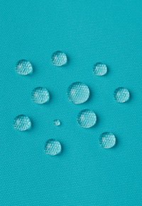 Turkusowa teksturowana powierzchnia z przezroczystymi kroplami wody o różnych rozmiarach odbijającymi światło, ukazująca wodoodporne właściwości materiału.