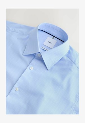 Hellblaues Baumwollhemd mit feinen vertikalen Nadelstreifen, spitzem Kragen und weißen Knöpfen. Das Etikett trägt die Aufschrift "NEXT COTTON STREET."