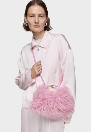 Femme portant des boucles d'oreilles créoles et une veste zippée rose clair, tenant un sac à main rose duveteux avec une bandoulière.