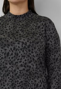 Bluzka z długim rękawem wykonana z miękkiej szarej tkaniny z czarnym wzorem w cętki lamparta, wysokim kołnierzem i luźnym krojem.