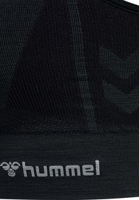 Tissu noir côtelé avec des motifs chevrons subtils et le logo blanc "hummel" tricoté sur le bord inférieur.