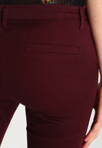 Bordeaux skinny broek gemaakt van rekbare stof met een achterzak en een gladde textuur. Heeft een aangesloten ontwerp en een gekleed uiterlijk.