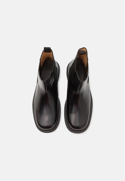 Botines de cuero negro hasta el tobillo con paneles laterales elásticos, superficie lisa, punta redondeada y un interior en contraste color tostado. Diseño minimalista.