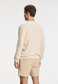 Light beige knit sweater with ribbed cuffs and hem, featuring a textured design, paired with light beige shorts.
