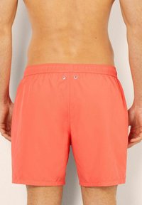 Swim trunks made of lightweight, coral fabric. Features elastic waistband with two metal eyelets at the back. Smooth texture and above-knee length.