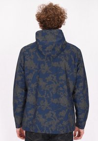 Giacca a vento navy con cappuccio caratterizzata da un motivo esagonale grigio. Il tessuto appare liscio con una vestibilità comoda e maniche lunghe.