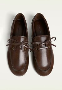 Scarpe in pelle marrone con punta rotonda, design con lacci, occhielli dorati e cuciture decorative lungo i bordi. Texture liscia complessiva.