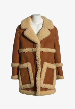 Manteau en shearling marron avec bordure en laine crème sur le col, les poignets, les poches et les bords avant sur un buste de mannequin blanc.