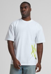 White short-sleeve t-shirt made of cotton, featuring a green abstract design on the left side and a small black label at the hem.