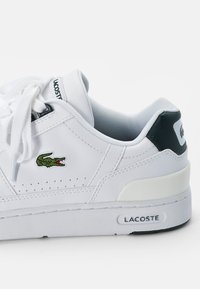 Białe sneakersy inspirowane lacrossem z zielonym akcentem, wyszywanym logo krokodyla, płaskimi sznurowadłami, perforowanymi detalami oraz amortyzowaną podeszwą.