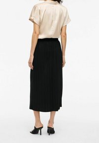 Gonna midi plissettata nera con vita elastica, abbinata a una blusa di raso beige chiara con maniche arrotolate e schiena con bottoni.
